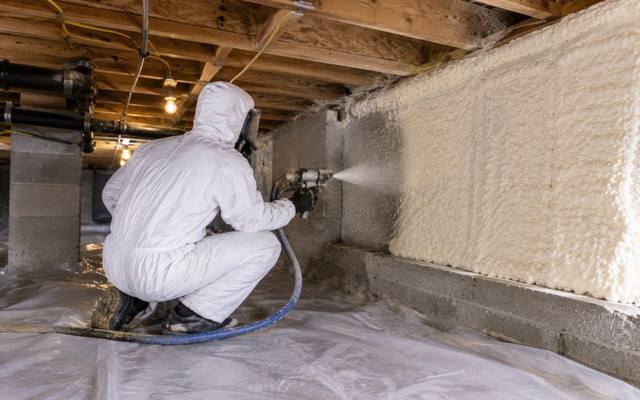 Installer working in a crawl space with foam on the walls
